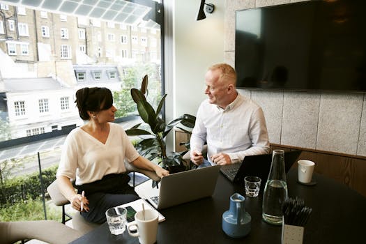 Two business professionals engaging in a team meeting in a modern London office with a large window view. Consultation